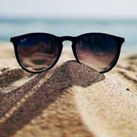 Sunglasses perched on a small heap of sand next to the sea. Image credit: Photo by Ethan Robertson on Unsplash